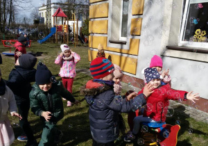 Widok na grupę bawiących się w ogrodzie przedszkolnym dzieci, które łapią bańki mydlane.